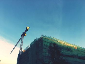 Low angle view of crane on building against sky