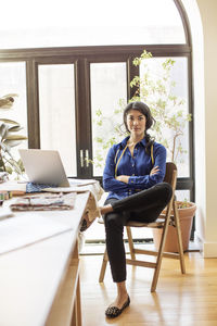 Portrait of confident fashion designer sitting arms crossed at office