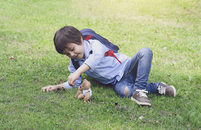 Boy with teddy bear sitting on grass