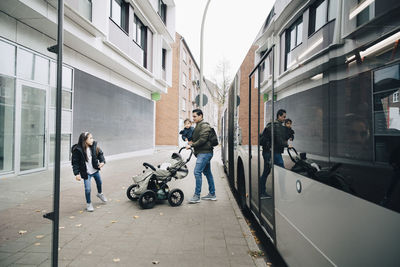 Father holding son walking with daughter on footpath against bus in city