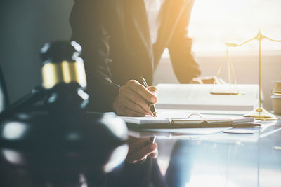 Midsection of lawyer writing in book at table in courthouse