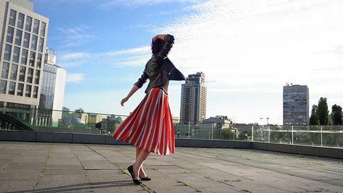 Happy woman wearing striped skirt and jacket on footpath in city