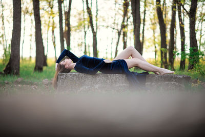 Side view of woman relaxing on tree trunk in forest