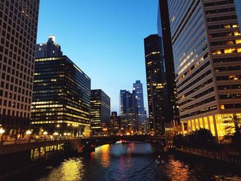 River amidst illuminated buildings against clear sky at dusk