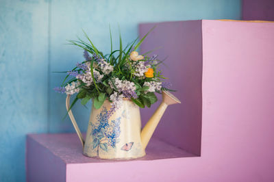 Artificial bouquet of flowers with green grass in an old vase in the shape of a watering can