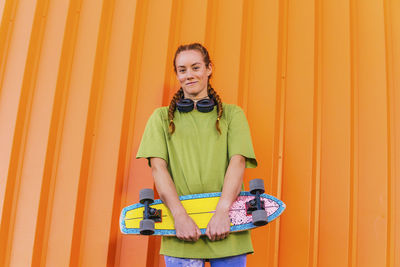 Portrait of a smiling young woman standing against yellow wall