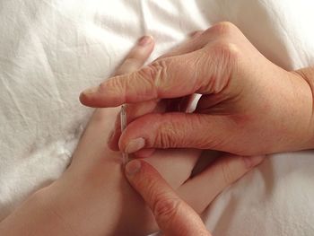 Close-up of woman giving acupuncture to customer on bed