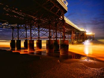 Illuminated pier over sea at sunset