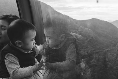 Cute baby by mother reflecting on overhead cable car window
