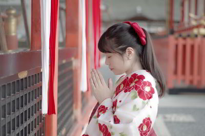 Side view of woman praying while standing indoors