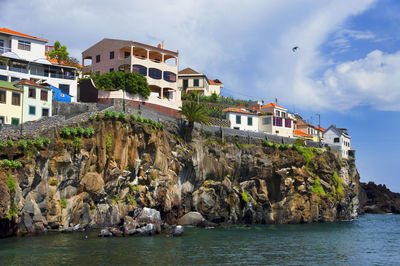 Low angle view of buildings on cliff by sea against sky