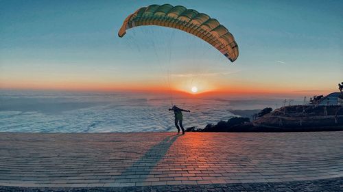 Low angle view of person paragliding over sea against sky during sunset