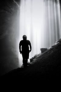 Man standing on rock formation against waterfall in cave