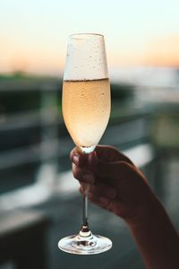 Close-up of hand holding wineglass against sky