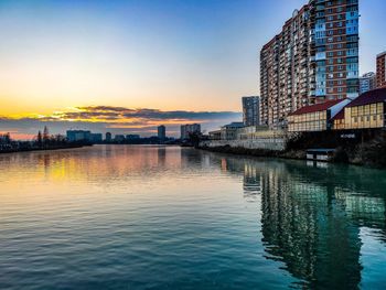 Scenic view of river by buildings against sky at sunset