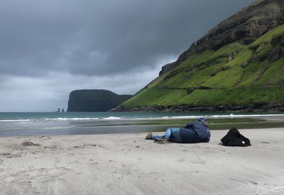 Man lying on beach against sky