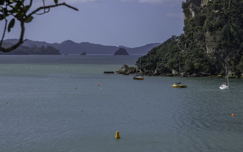 Scenic view of three sailboats in a secluded bay against wooded cliffs with islands on a sunny day