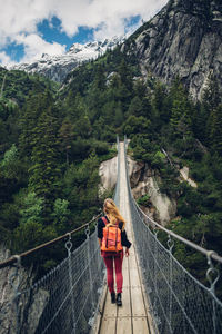 Rear view of woman walking on footbridge against mountain