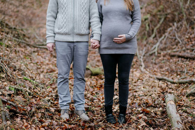 Low section of couple standing on autumn leaves in forest