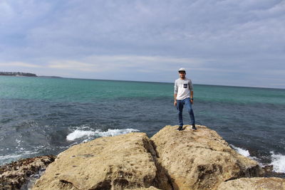 Full length of man standing on rock by sea against sky