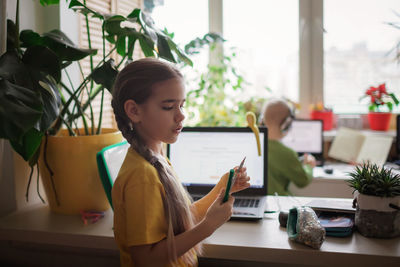 Cute girl holding pencil standing at classroom