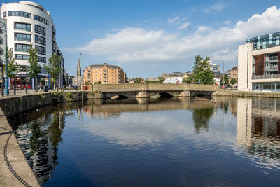 Arch bridge over river by buildings in city against sky