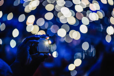 Cropped hands of man photographing against illuminated lights at night