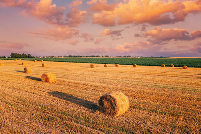 Hay bales on field against sky during sunset