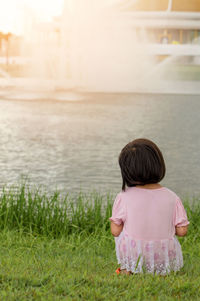 Rear view of girl sitting on grass by lake