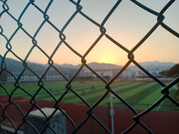 Close-up of chainlink fence against sky during sunset