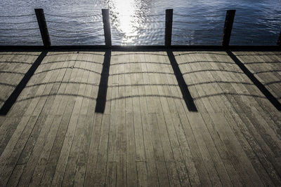 Shadow of railing on pier by sea against sky