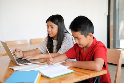 Siblings sitting on table at home