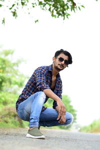 Young man wearing sunglasses crouching on road