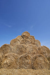 Hay bales on field against blue sky