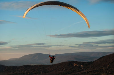 Man paragliding over mountains against sky