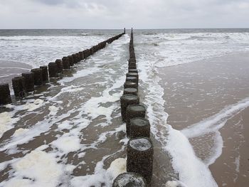 Wooden posts in sea against sky during winter