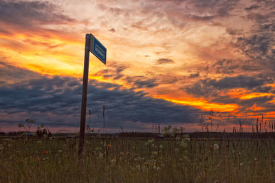 Road sign on field against sky at sunset