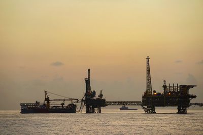 Oil rig in sea against sunset sky