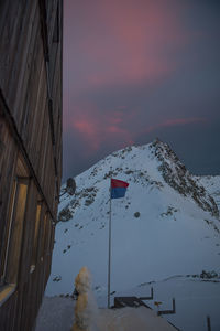 Snow covered buildings against sky during sunset