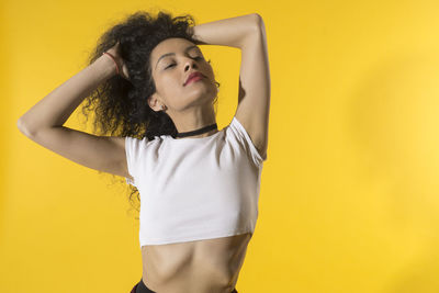 Portrait of young woman standing against yellow background