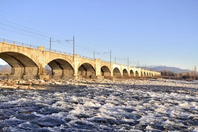 Arch bridge over piave river against clear sky during winter