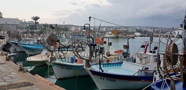 Boats moored at harbor in city against sky