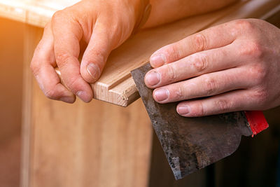 Close-up a carpenter in work clothes restoring a wood with a spatula on a wooden table. 