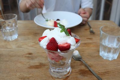 Midsection of man eating strawberry dessert with friend in cafe