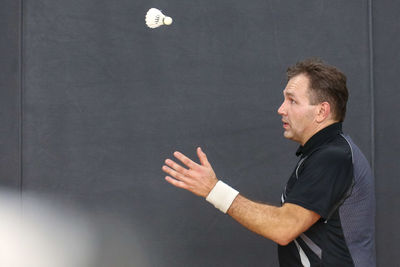 Side view of mature man looking at shuttlecock against wall