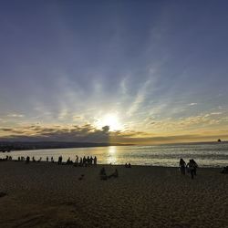 People on beach against sky during sunset