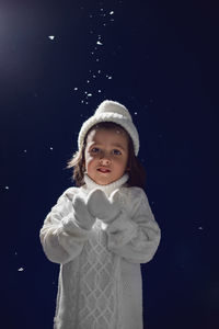 Boy in a white knitted sweater and hat catches snow on the street at night lantern on christmas day