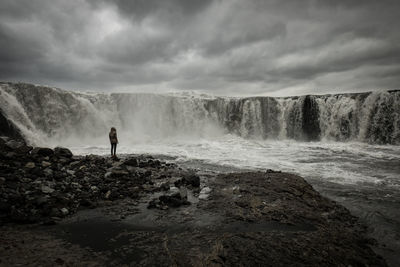 Rear view of man standing by waterfall against sky