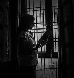 Side view of woman looking through window at home