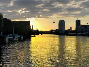 Scenic view of river by buildings against sky during sunset